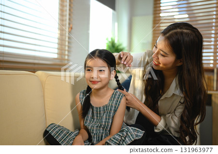 The mother is lovingly styling her daughter's hair The girl is sitting on a couch and smiling, Scene is happy and friendly The mother is lovingly styling her daughter's hair The girl is sitting on a couch and smiling, Scene is happy and friendly 131963977