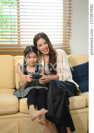 Mother teaching her daughter how to play a video game, sharing laughter and learning through fun digital playtime 131963980
