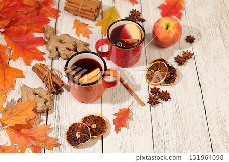 Seasonal abstract composition with enamel mugs with hot autumn drink, mulled wine with apples and fallen leaves, star anise and cinnamon, banner for screen, autumn greeting concept, mockup for menu. 131964098