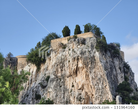 A scenic ancient fortress atop a rocky outcrop surrounded by lush, green vegetation 131964160