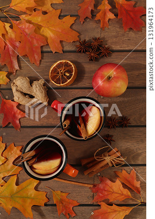 Seasonal abstract composition with enamel mugs with hot autumn drink, mulled wine with apples and fallen leaves, star anise and cinnamon, banner for screen, autumn greeting concept, mockup for menu. 131964173