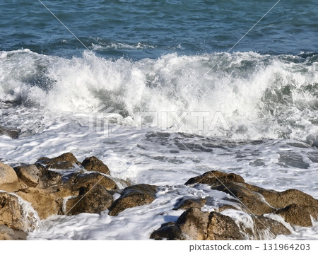 The Waves Are Powerfully Crashing Against the Rocky Shoreline, Creating a Stunning Scene 131964203