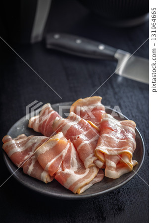 Slices of raw bacon on plate on black table. 131964665