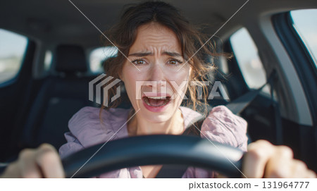 terrified woman's face while driving a car. Her mouth is open in a scream of panic, eyes wide with fear, gripping the steering wheel. The image captures a moment of intense stress and danger. 131964777