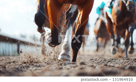 powerful legs of racehorses at a full gallop, kicking up a dramatic spray of dirt and sand. The motion blur and focus on the foreground convey speed, action, and the intensity of the competition 131964910