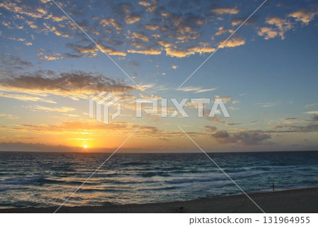 Golden sunrise over the ocean with gentle waves and scattered clouds, viewed from a beach at horizon level, creating a serene and tranquil coastal scene Golden sunrise over the ocean with gentle waves and scattered clouds, viewed from a beach at horizon level, creating a serene and tranquil coastal scene 131964955