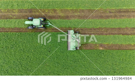Tractor cutting grass in a lush green field during daytime 131964984
