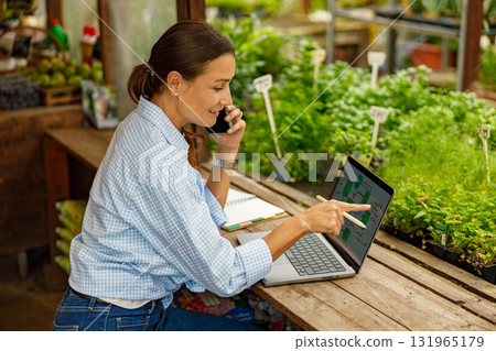 A woman is actively working in a greenhouse while using her laptop for various tasks and projects A woman is actively working in a greenhouse while using her laptop for various tasks and projects 131965179