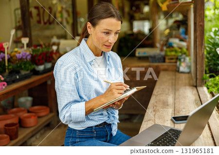 A Young Woman is Engaged in Working on Her Laptop in a Cozy Plant Shop Environment A Young Woman is Engaged in Working on Her Laptop in a Cozy Plant Shop Environment 131965181