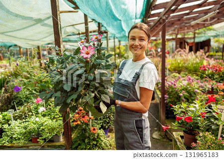 A Beautiful Gardener Holding a Vibrant Flower Inside a Lush Greenhouse Environment 131965183