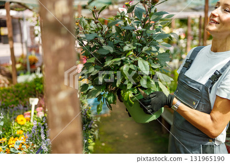 A woman is joyfully tending to an array of vibrant plants inside a colorful flower shop A woman is joyfully tending to an array of vibrant plants inside a colorful flower shop 131965190