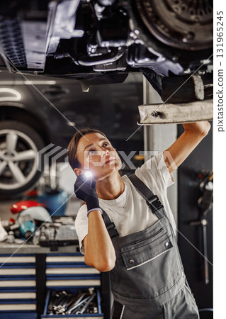 A Female Mechanic Diligently Working Underneath a Car in a WellEquipped Workshop Setting A Female Mechanic Diligently Working Underneath a Car in a WellEquipped Workshop Setting 131965245
