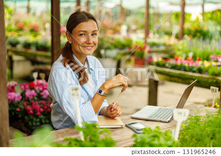 A Happy Woman is Working Enthusiastically in a Colorful Flower Shop with Her Laptop A Happy Woman is Working Enthusiastically in a Colorful Flower Shop with Her Laptop 131965246