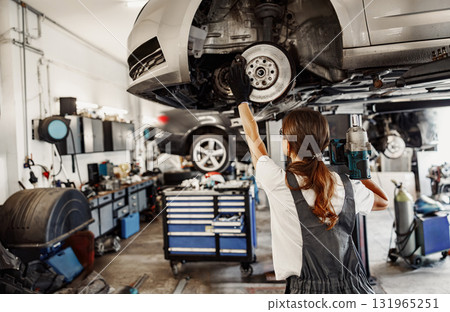 An Automotive Mechanic is diligently working on a car using a lift in the garage environment 131965251