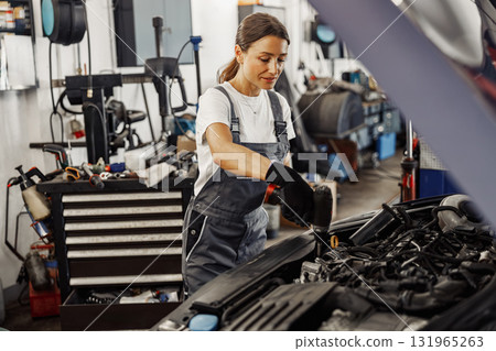 A skilled woman mechanic is diligently working on a car engine inside a garage setting 131965263