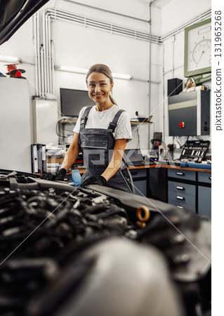 A hardworking female mechanic skillfully working on a car engine inside a garage setting A hardworking female mechanic skillfully working on a car engine inside a garage setting 131965268