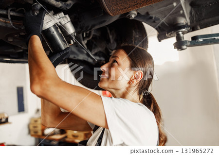 A highly skilled woman is expertly performing automotive maintenance work in a workshop environment 131965272