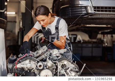 A skilled female mechanic is diligently working on an engine within her garage workshop 131965298