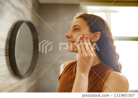 A Young Woman Enjoys Applying Skincare in a Modern, Stylish Bathroom that Exudes Elegance A Young Woman Enjoys Applying Skincare in a Modern, Stylish Bathroom that Exudes Elegance 131965307