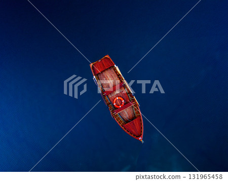 A breathtaking Aerial View capturing a Solitary Red Boat floating gracefully on Deep Blue Water A breathtaking Aerial View capturing a Solitary Red Boat floating gracefully on Deep Blue Water 131965458