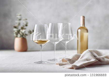 Elegant wine still life featuring three glasses, one filled with white wine, and a bottle against a textured backdrop. Ideal for beverage, lifestyle, or celebratory concepts. Elegant wine still life featuring three glasses, one filled with white wine, and a bottle against a textured backdrop. Ideal for beverage, lifestyle, or celebratory concepts. 131966669
