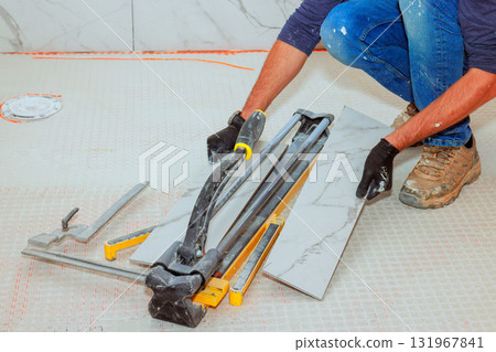 Construction worker carefully cuts ceramic tiles with tile cutter, preparing for installation. 131967841