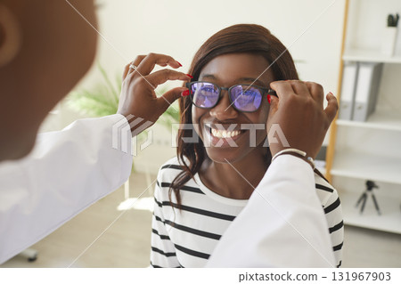 Optometrist puts new glasses on eyes of dark-skinned woman for testing and trying on. Optometrist puts new glasses on eyes of dark-skinned woman for testing and trying on. 131967903