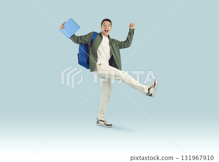Happy excited student boy holding textbook with backpack isolated on blue studio background. 131967910