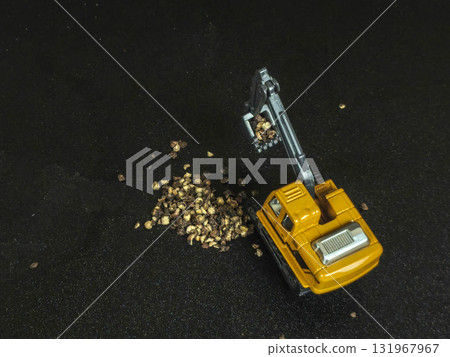 Toy excavator digging into a pile of coarse pepper on a black background. 131967967