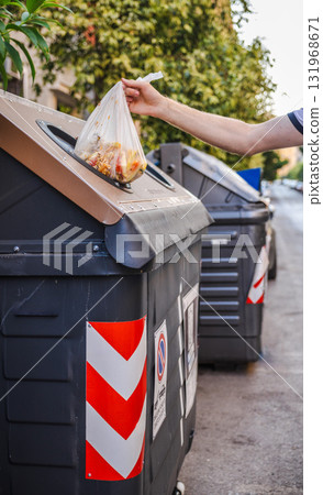 Man placing a plastic bag with food scraps into a compost bin on a Roman street, emphasizing eco-friendly waste management and urban environmental responsibility. Man placing a plastic bag with food scraps into a compost bin on a Roman street, emphasizing eco-friendly waste management and urban environmental responsibility. 131968671