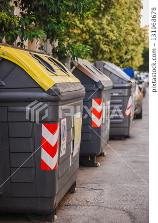 Row of recycling containers on a residential street in Rome, Italy, with yellow and brown lids for sorting waste, promoting urban environmental responsibility and sustainability. 131968678