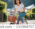 A woman happily pedaling a bicycle on a slope in a town surrounded by nature 131968757