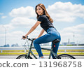 A woman with long brown hair pedaling a bicycle under the blue sky 131968758