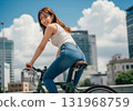 A woman riding a bicycle with summer city buildings in the background 131968759