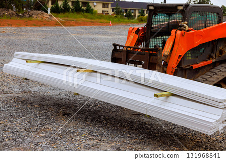 Construction vehicle lifts long white sheets of material at job set 131968841