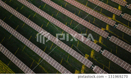 Aerial top view of solar panels arranged in diagonal rows on a green field, producing renewable electricity under sunlight. Aerial top view of solar panels arranged in diagonal rows on a green field, producing renewable electricity under sunlight. 131969270