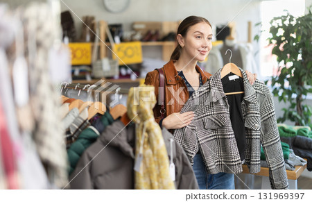 Positive young woman choosing winter coat in clothing store 131969397