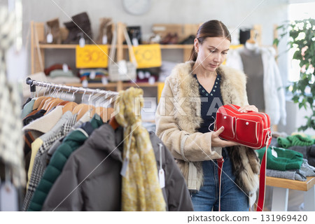 Hesitant young woman choosing handbag in clothing store Hesitant young woman choosing handbag in clothing store 131969420