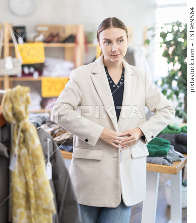 Glad young woman trying on winter coat in clothing store 131969564