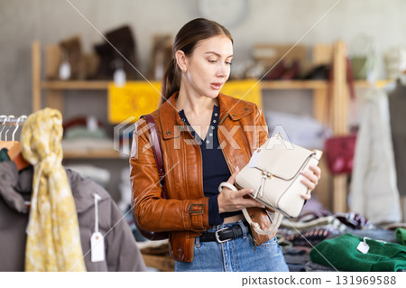 Hesitant young woman choosing handbag in clothing store Hesitant young woman choosing handbag in clothing store 131969588
