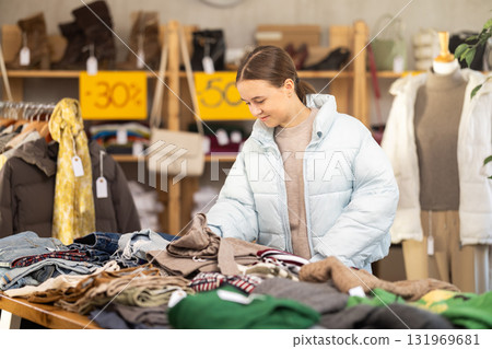 Focused young teen female client carefully choosing pants or stylish trousers in clothing mall. Black Friday sale of winter clothing collection Focused young teen female client carefully choosing pants or stylish trousers in clothing mall. Black Friday sale of winter clothing collection 131969681