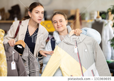 Mom and teenage daughter choosing down jacket in clothing store Mom and teenage daughter choosing down jacket in clothing store 131969695