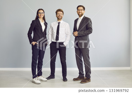 Three cheerful business people standing isolated on grey background and looking at camera. 131969792