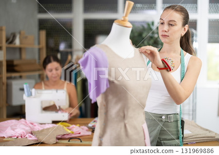 Young female dressmaker working with mannequin while other sews 131969886
