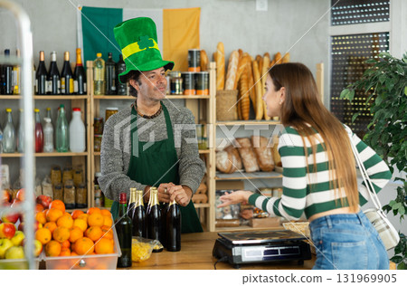 Salesman in green leprechaun hat serving beer to female shopper Salesman in green leprechaun hat serving beer to female shopper 131969905
