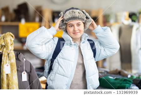 Positive teen girl customer choosing winter fur hat for cold season in clothing market Positive teen girl customer choosing winter fur hat for cold season in clothing market 131969939