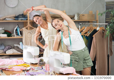 Female dressmakers doing a warm-up in the workshop in summer Female dressmakers doing a warm-up in the workshop in summer 131970000