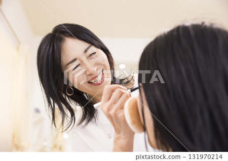 A middle-aged female makeup artist applying makeup to a young woman A middle-aged female makeup artist applying makeup to a young woman 131970214