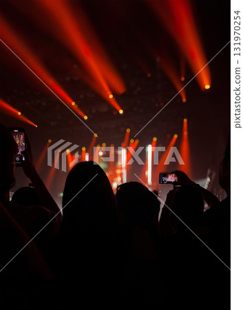 Pop music concert with scene stage lights in red tones. Black silhouettes of fans in the foreground 131970254