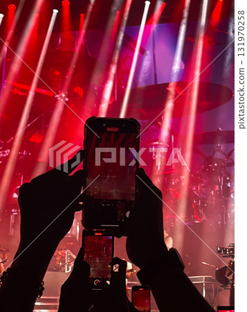 Hands holding smartphones and recording at a rock concert with red stage lights. Hands holding smartphones and recording at a rock concert with red stage lights. 131970258